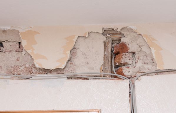 Freigelegte alte Stromleitungen und bröckelnder Putz an einer Wand während einer Altbausanierung.