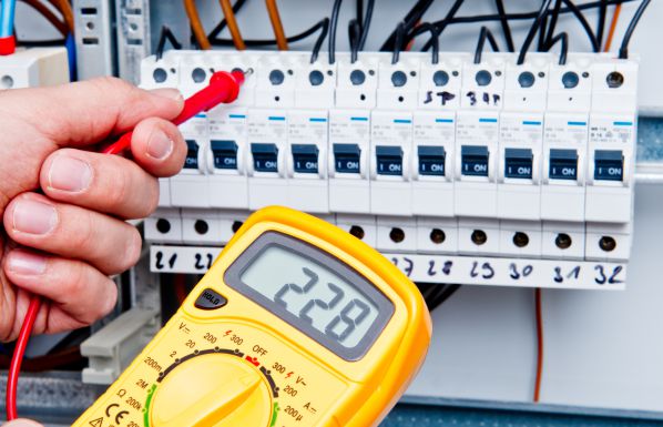 Elektriker misst Spannung an einem Sicherungskasten mit einem digitalen Multimeter, DGUV V3 Prüfung zur Betriebssicherheit elektrischer Anlagen.