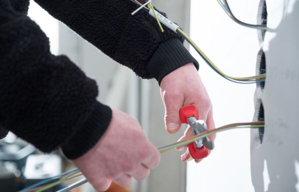Elektriker verlegt und installiert Stromleitungen in einem Neubau, Detailaufnahme von Kabeln und Werkzeug bei der Arbeit.
